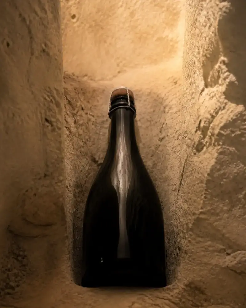 Bouteille sombre de vin effervescent couchée dans une cave de craie, éclairage chaud, aucune étiquette lisible