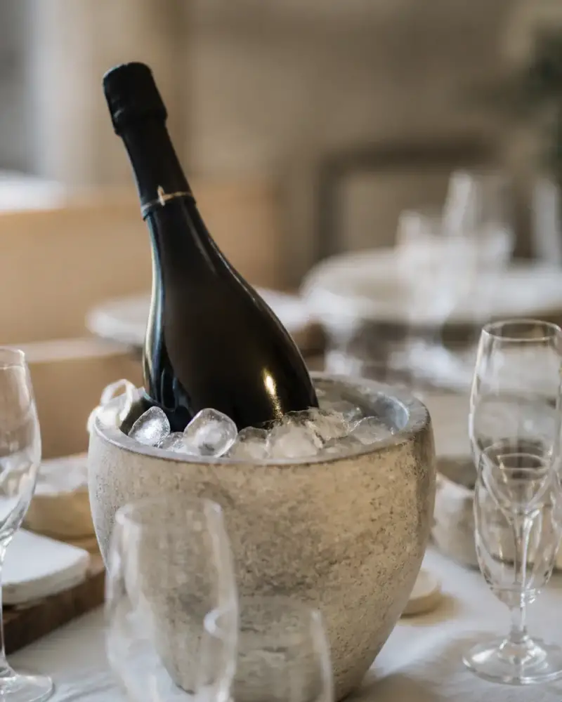 Bouteille de champagne de grand format posée dans un seau rempli de glace sur une table dressée, avec des flûtes autour