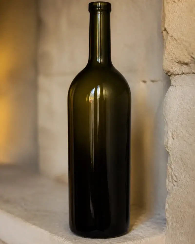 Bouteille de vin en verre vert foncé sans étiquette posée sur une étagère en pierre, éclairage chaud