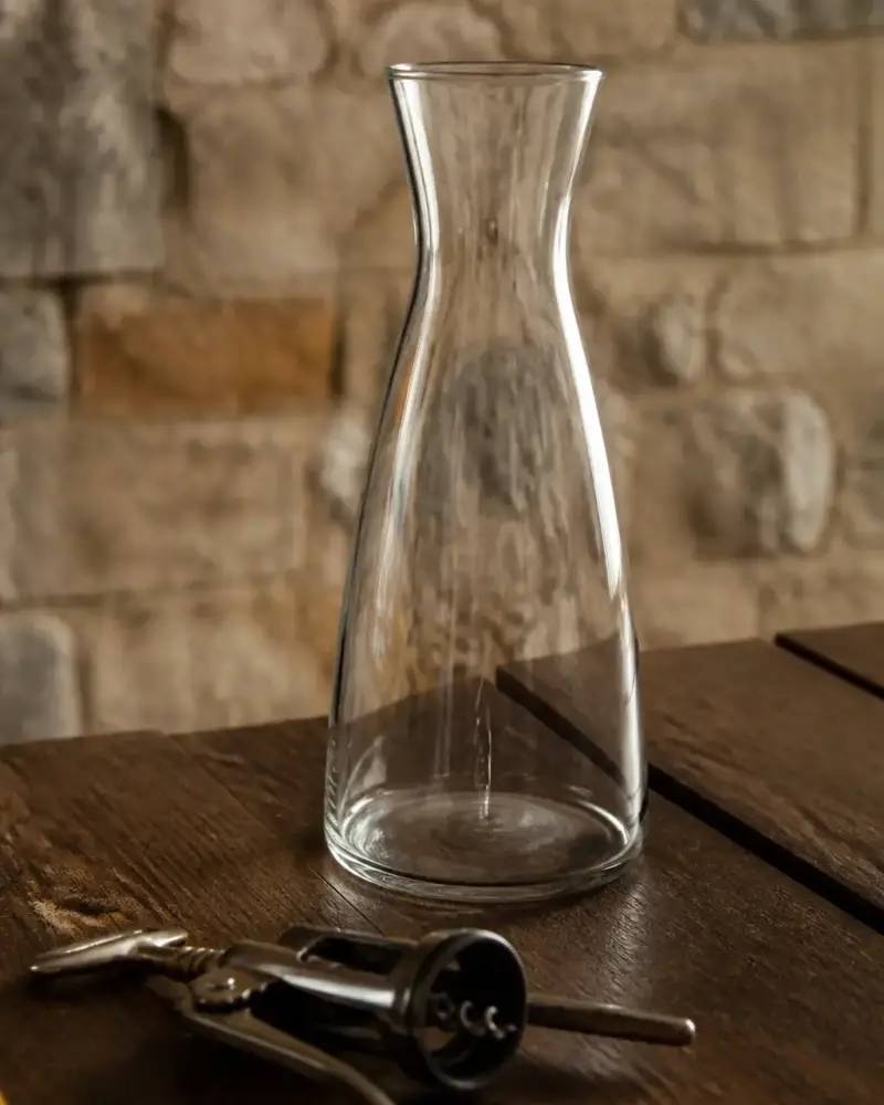 Carafe en verre transparent vide et tire-bouchon posés sur une table en bois sombre, lumière chaude